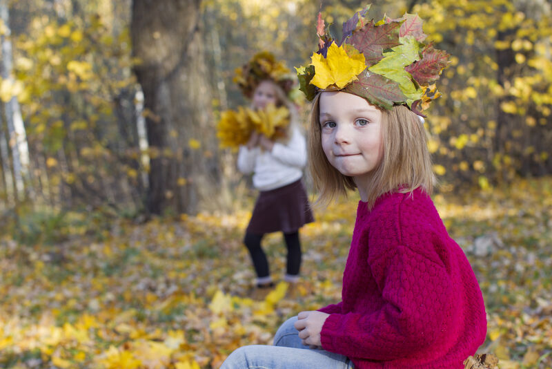 Mädchen im roten Pullover mit Krone aus Herbstlaub im herbstlichen Wald