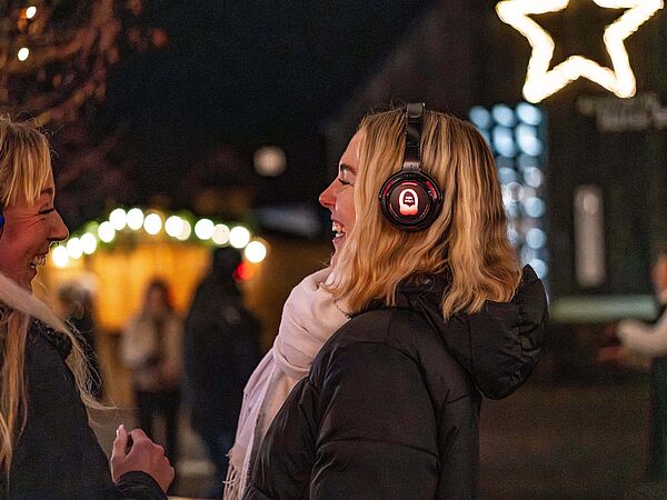 Silent Disco zum Weihnachtsmarkt auf Gut Herbigshagen Zwei junge Frauen mit Kopfhörern vor weihnachtlicher Hofkulisse