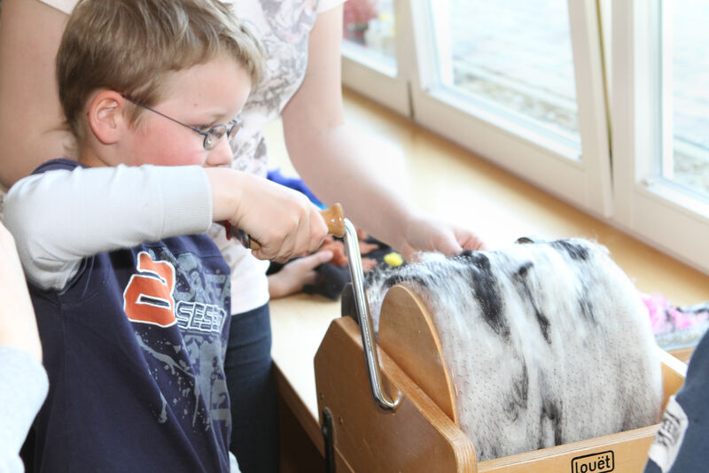 Kind dreht an Kurbel einer Filzrolle zur Wollverarbeitung im Kreativraum des Natur-Erlebnishauses