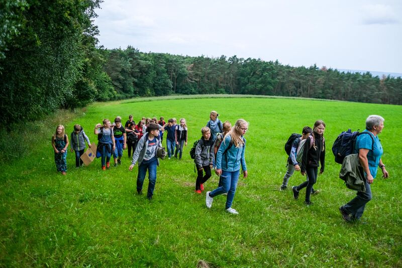 Schüler Wandergruppe mit Rucksäcken auf grüner Wiese mit Wald im Hintergrund