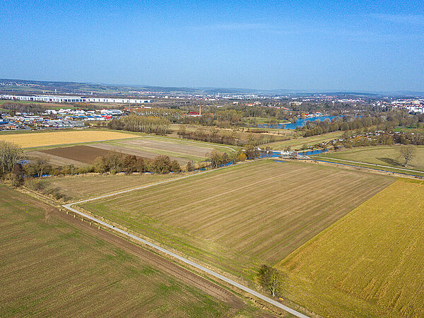 Aus der Vogelperspektive sieht man die noch intensiv genutzte Ackerfläche. Links und rechts sind weitere intensiv genutzte Ackerflächen. Am Horizont befinden sich einige Gebäude der Stadt Göttingen. Die Leine fließt durch dieses Areal.
