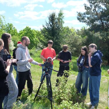 Eine Gruppe von Jugendlichen steht auf einer Wiese um eine Filmkamera herum