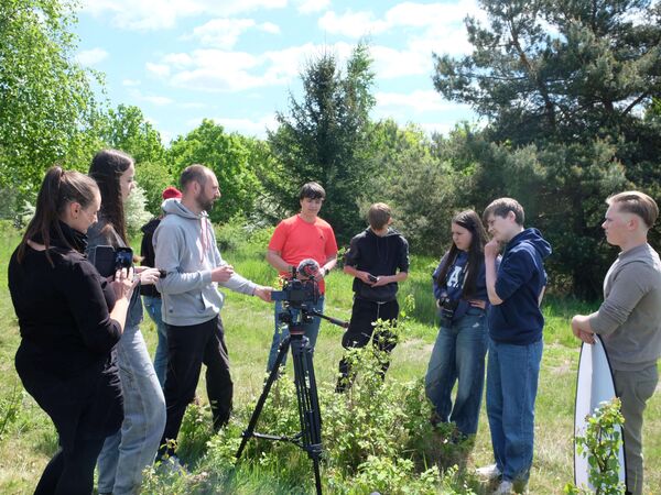 Gruppe von Schülerinnen und Schülern beim Medienprojekt GreenCut-JUMP am Grünen Band Eichsfeld Eine Gruppe von Jugendlichen steht auf einer Wiese um eine Filmkamera herum