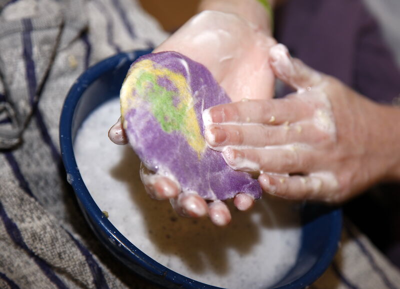 Rundes Filzobjekt in lila und grün wird per Hand mit Seifenwasser eingerieben