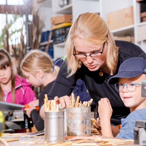 In der Werkstatt werden Nisthilfen gebaut, Person erklärt Kind, wie das Material in die Blechdose geschichtet wird