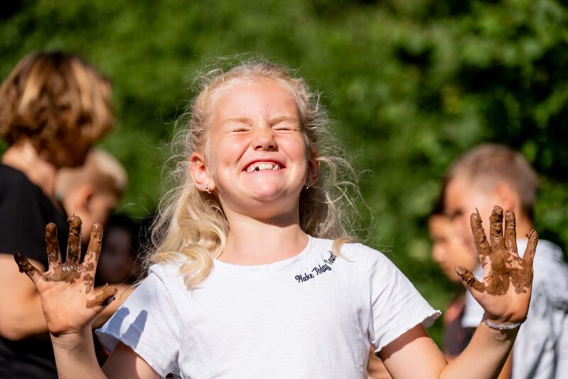 Mädchen lacht, Hände sind voller Lehm